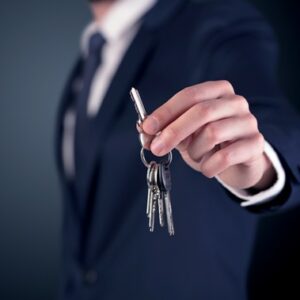 Young businessman hand over keys with empty dark background